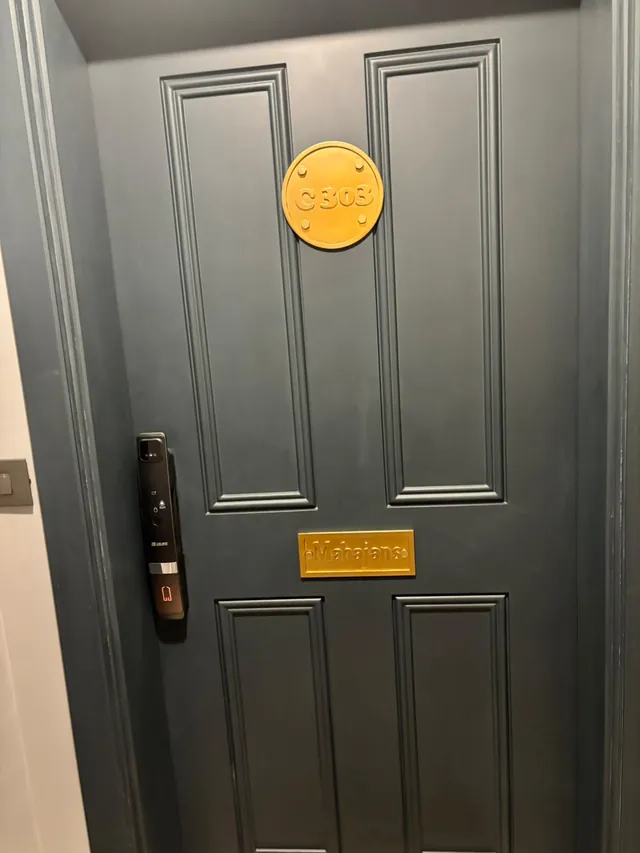 Dark grey panelled front door with a round brushed-brass C303 number plate and a brass Mahajans name plate