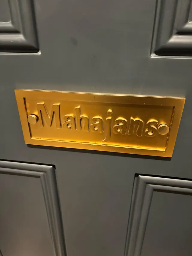 Finished brushed-gold Mahajans name plate with raised letters on a dark grey panelled door