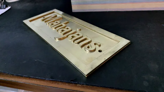 Raw brass name plate with raised letters on the workshop bench, seen at an angle