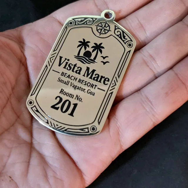 Vista Mare brass room key tag held in an open hand to show its size